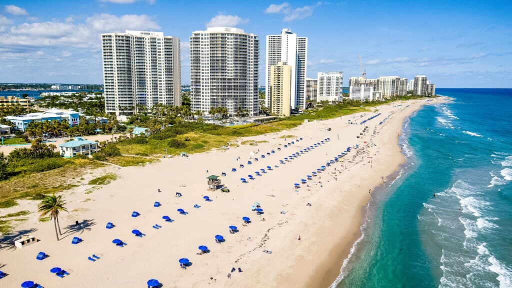 High-rise condominiums and beachfront with blue umbrellas on a sunny day in Palm Beach, Florida, near Palm Beach bail bonds offices.